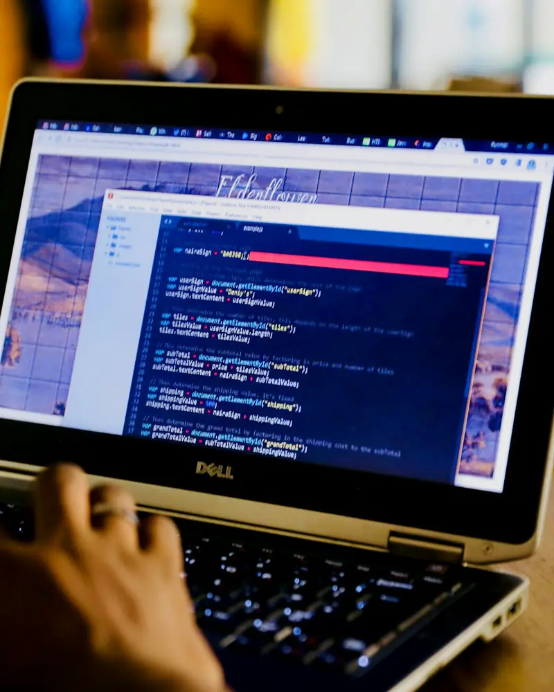 Mains sur le clavier d’un ordinateur portable, du code à l’écran à côté de la maquette d’un site